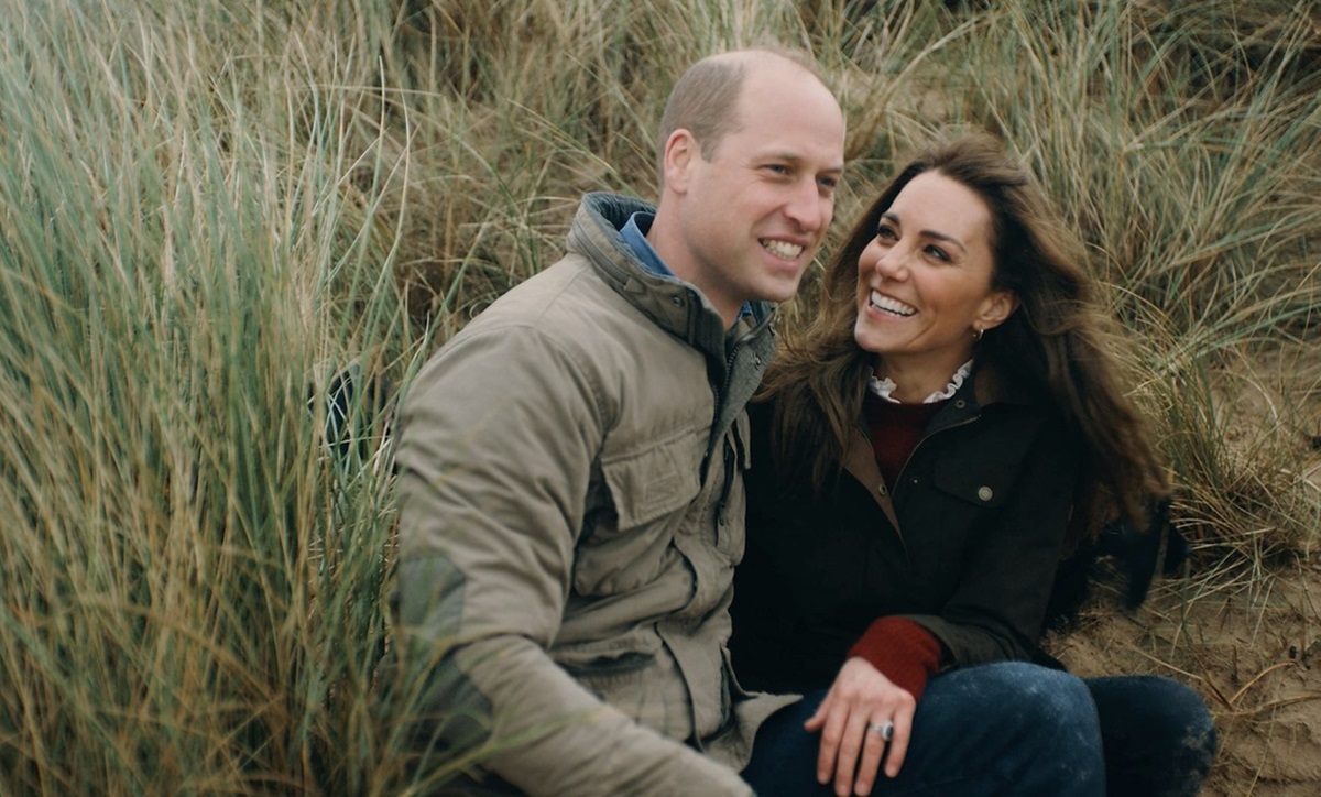 Prințul William și Kate Middleton în timp ce se țin în brațe și pozează pe jos, într-un stufăriș