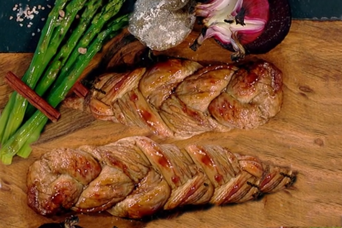 Două bucăți de friptură din mușchiuleț de porc împletit alături de sparanghel verde și ceapă roșie