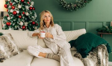 O femeie frumoasă care paortă o pijama albă și stă singură pe o canapea în fața bradului de Crăciun