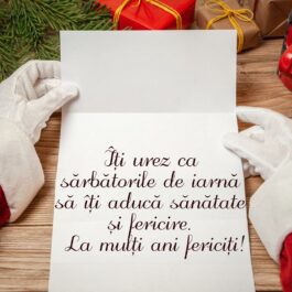 Mâinile cu mănuși ale lui Moș Crăciun care țin în mână o scrisoare cu mesaje de Crăciun