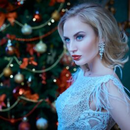 O femeie frumoasă care poartă o rochie albă și stă în fața unui brad de Crăciun pentru a ilustra una dintre cele trei zodii care pierd bani în luna decembrie 2023