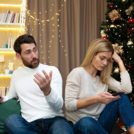 Un cuplu care stă spate în spate în timp ce se uită pe telefon pentru a ilustra zodiile care urăsc Crăciunul