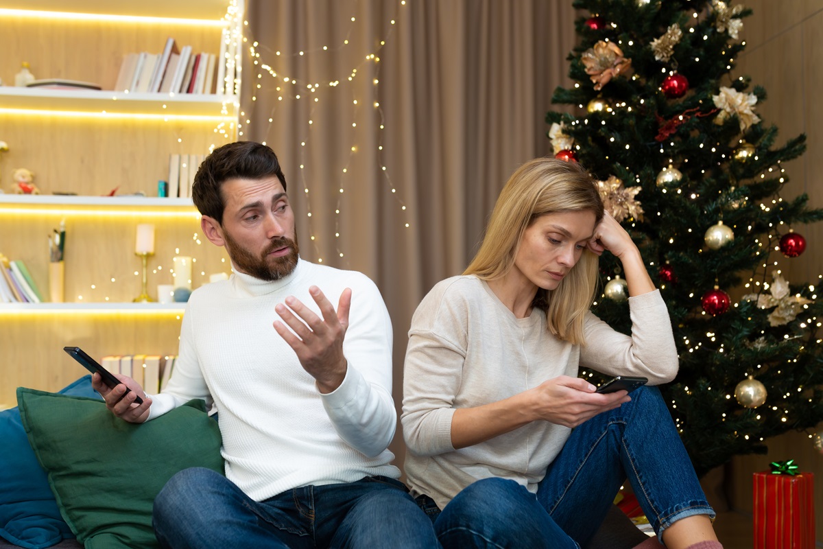 Un cuplu care stă spate în spate în timp ce se uită pe telefon pentru a ilustra zodiile care urăsc Crăciunul