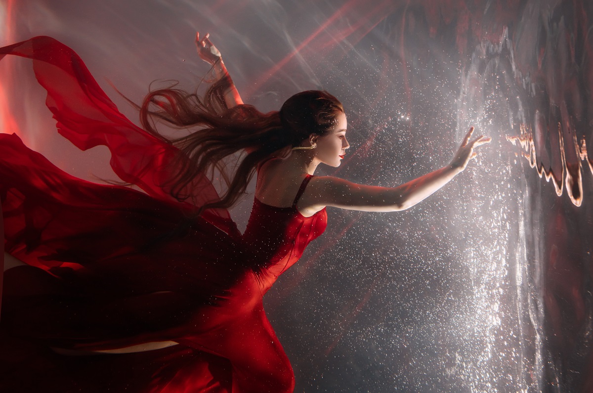 O femeie frumoasă care poartă o rochie roșie și se află sub apă pentru a ilustra zodiile norocoase ale zilei de 24 decembrie 2023