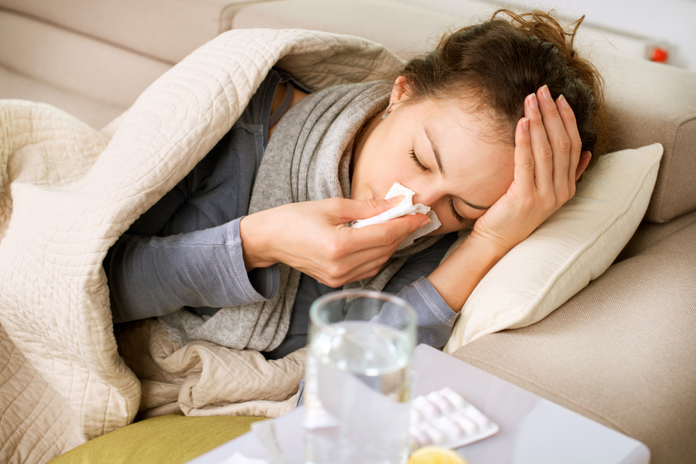 O femeie care este răcită, stă pe canapea și își suflă nasul