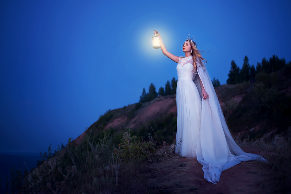 O femeie îmbrăcată în rochie albă, pe un deal, cu un felinar în mână