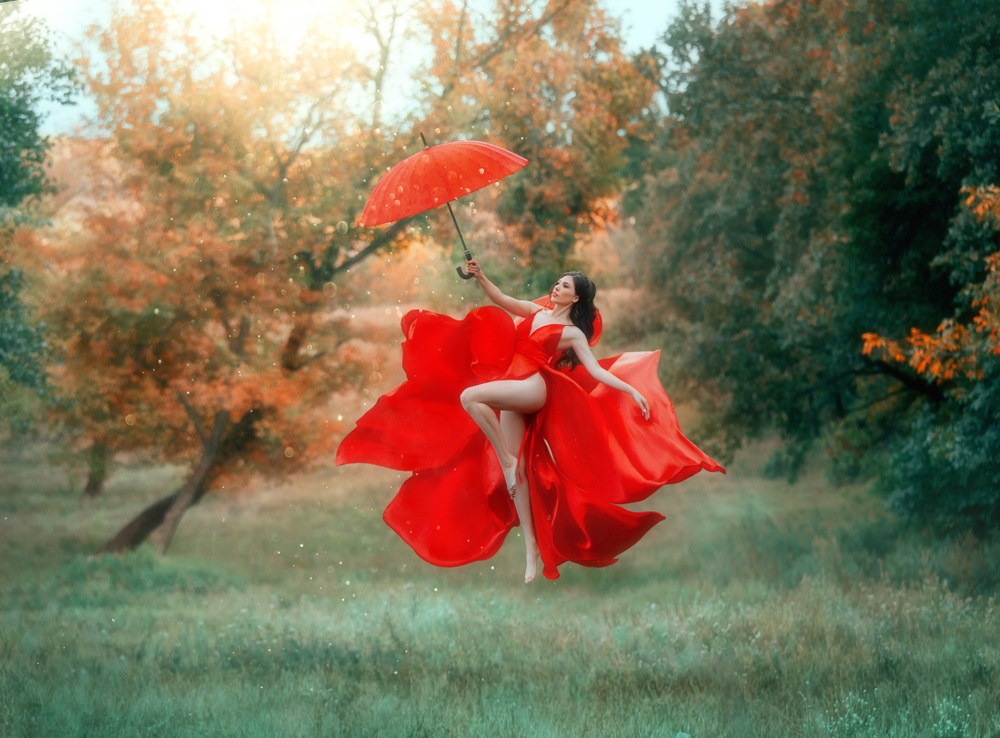O femeie îmbrăcată în rochie roșie, care dansează cu o umbrelă