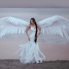 O femeie la malul mării, în rochie de mireasă, cu aripi de înger