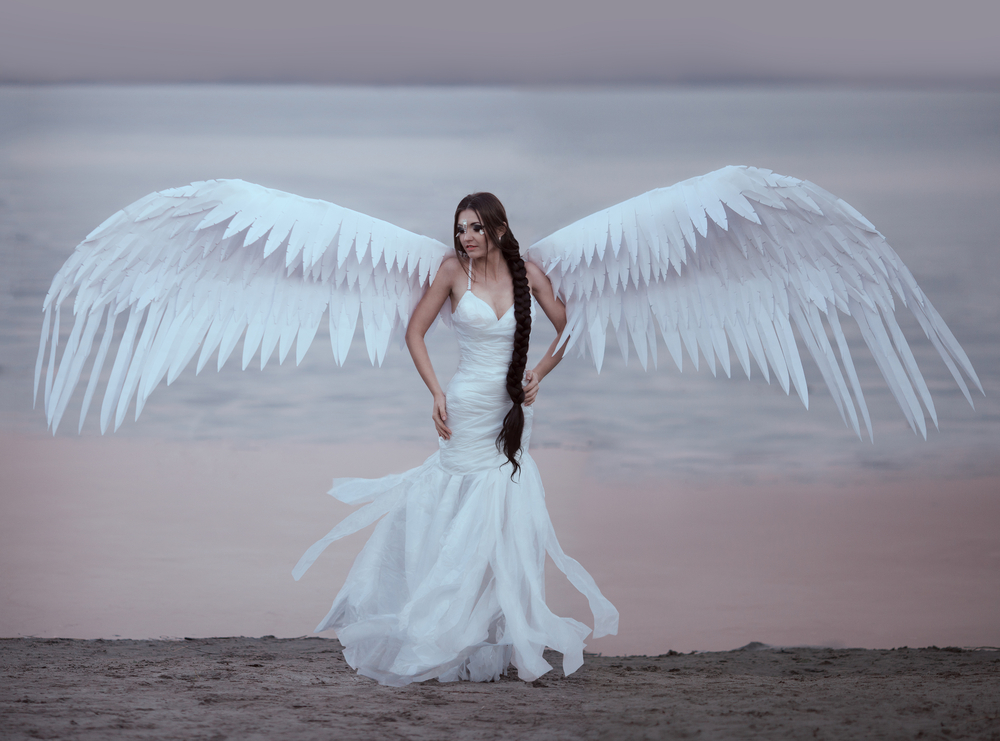 O femeie la malul mării, în rochie de mireasă, cu aripi de înger