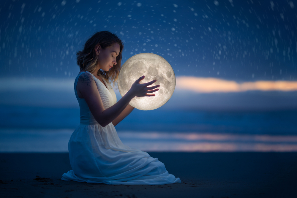 O femeie în rochie albă care ține în mână o Lună mare
