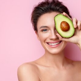 O femeie frumoasă care ține în fața feței o jumătate de avocado
