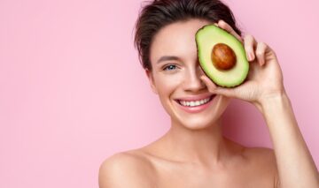 O femeie frumoasă care ține în fața feței o jumătate de avocado