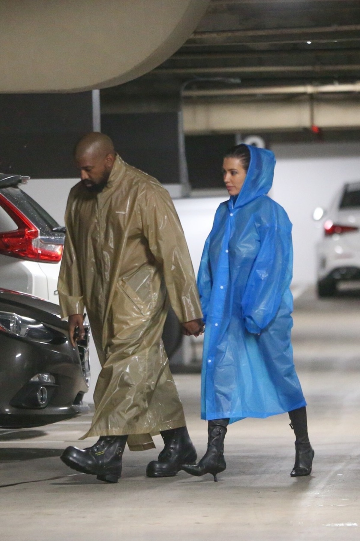 Kanye West într-o pelerină de ploaie maro și Bianca Censori într-o pelerină de ploaie albastră