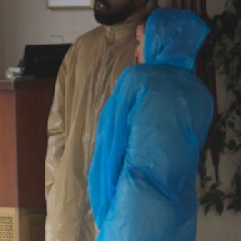 Bianca Censori într-o pelerină de ploaie albastră în timp ce vorbește cu Kanye West