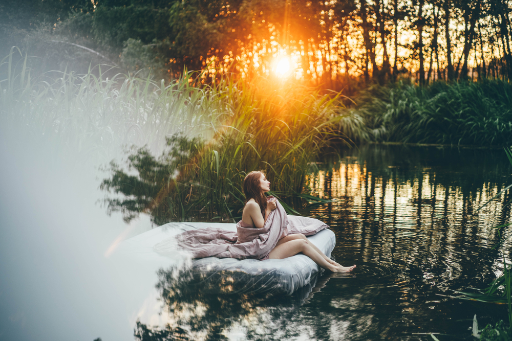 Fată care doarme pe un pat așezat pe un lac cu un soare care apune