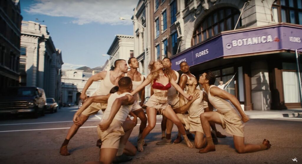 Jennifer Lopez în timp ce dansează cu un grup de bărbați în videoclipul melodiei Can't Get Enough