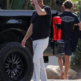 Kevin Costner, într-un tricou negru și pantaloni albi, la mașină, în parcare