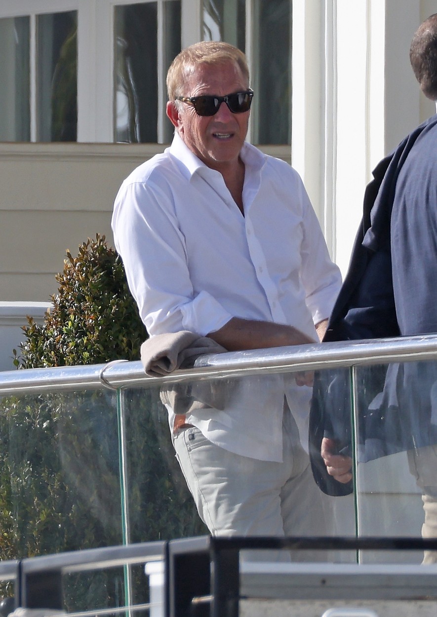 Kevin Costner, pe balconul unei clădiri, în haine de culoare albă