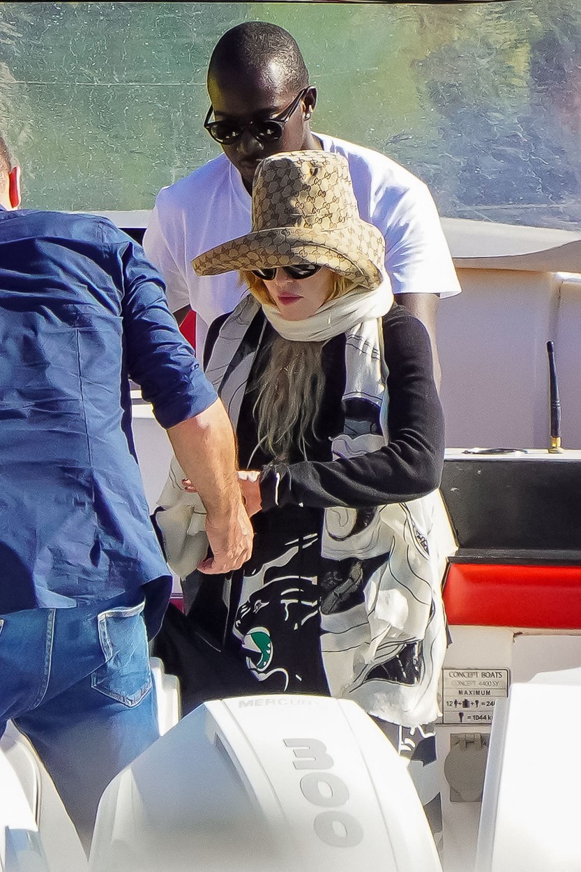 Madonna, cu pălărie și ochelari de soare, ajutată de cineva din echipa sa