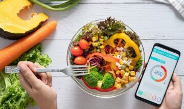 Un bol plin cu legume sănătoase alături de două mini care țin o furculiță și un telefon care numără caloriile