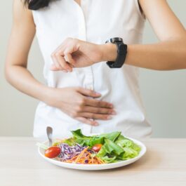 O femeie care se uită la ceas în timp ce are în față o salată