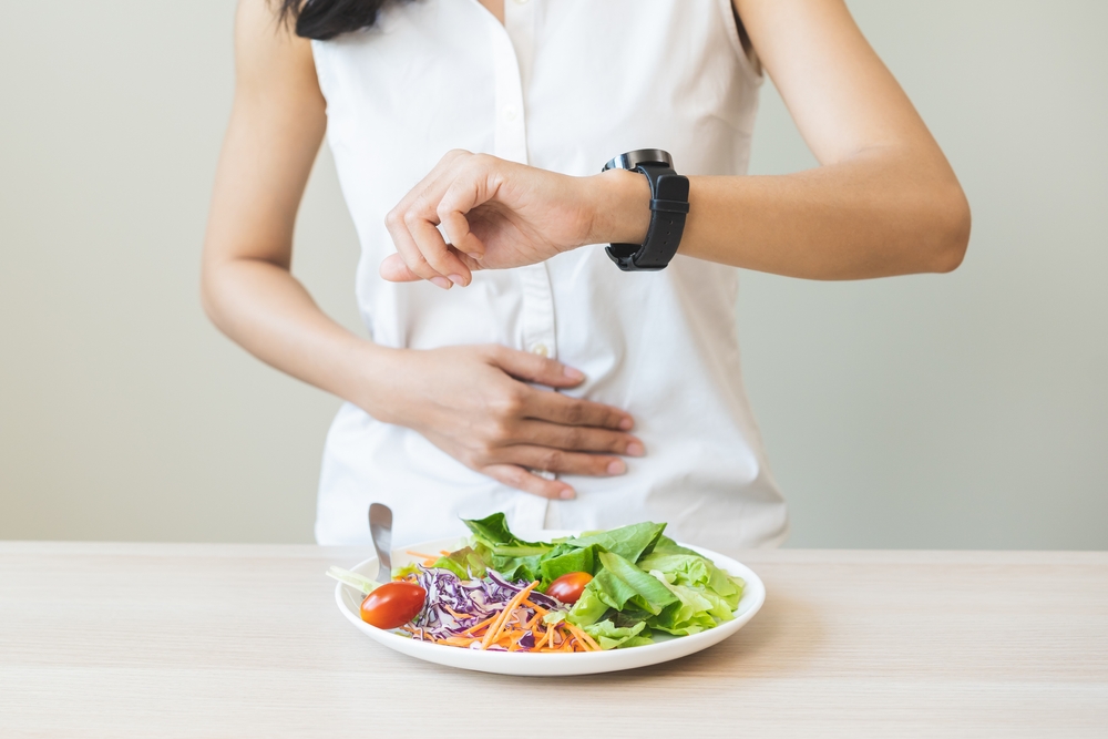 O femeie care se uită la ceas în timp ce are în față o salată