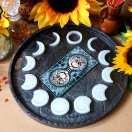 O tavă pe care se află două cărți de tarot și mai multe lumânări albe care ilustrează fazele lunii, înconjurată fiind de mai multe flori de Floarea-Soarelui