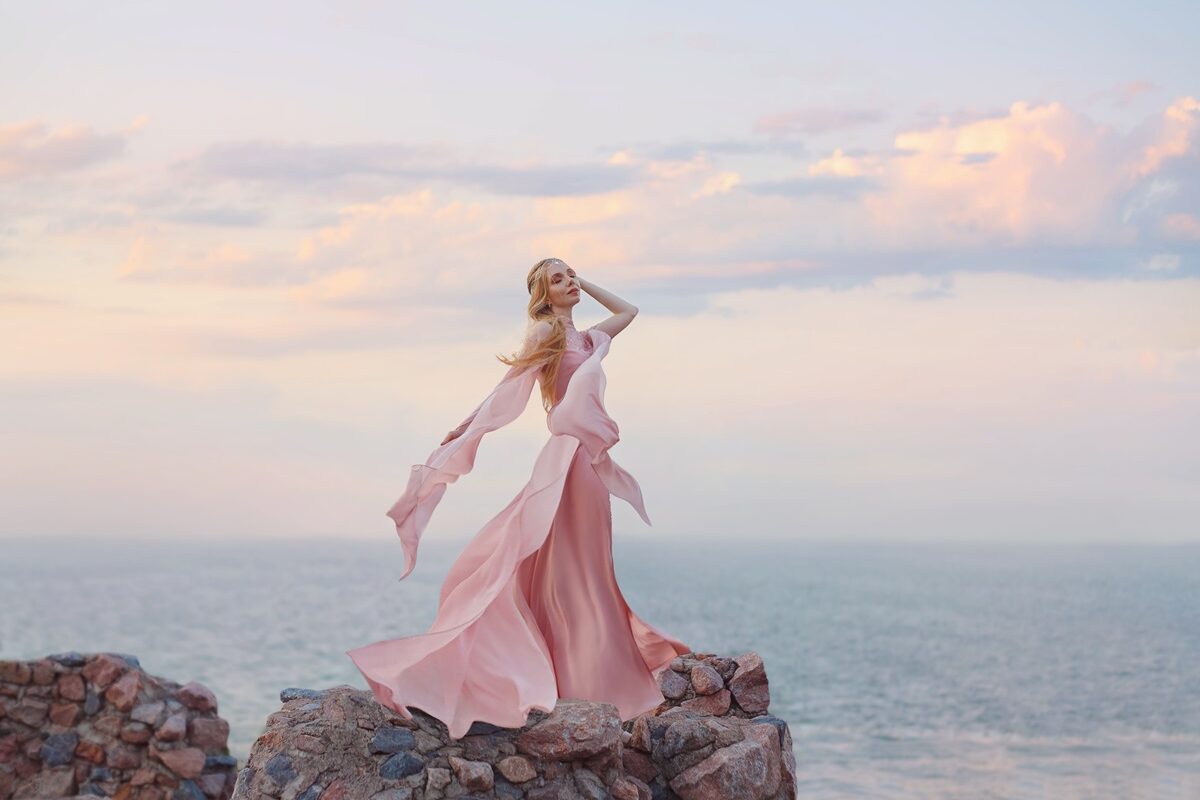 O femeie frumoasă care stă pe o stâncă întro rochie roz și privește marea ilustrând una dintre cele trei zodii care au un spirit liber