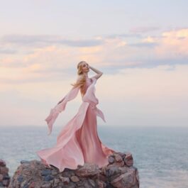 O femeie frumoasă care stă pe o stâncă întro rochie roz și privește marea ilustrând una dintre cele trei zodii care au un spirit liber