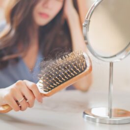 O femeie care stă în fața oglinzii cu o perie plină de păr