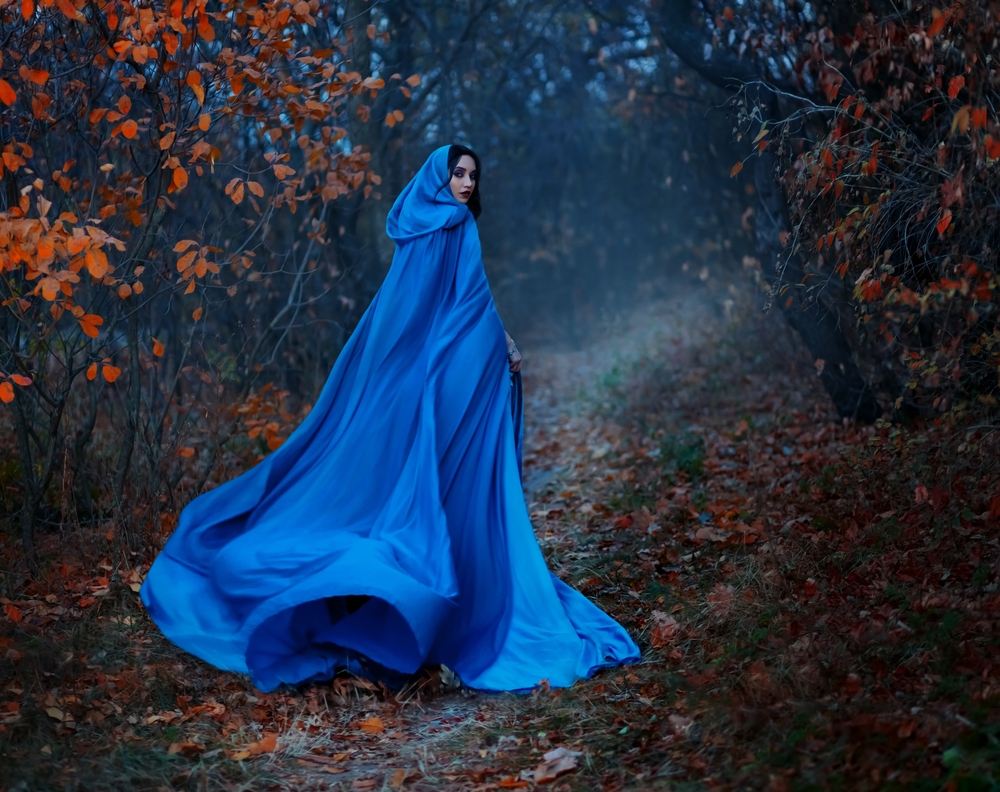 O femeie într-o rochie cu pelerină albastră, într-o pădure