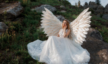O femeie în rochie de mireasă, cu aripi de înger, pe o stâncă