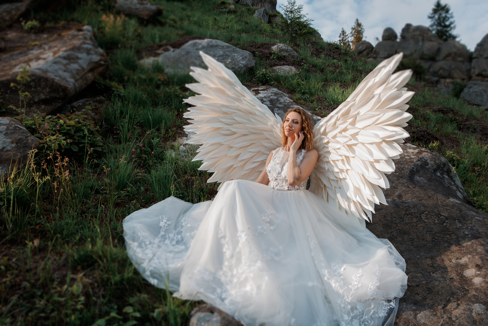 O femeie în rochie de mireasă, cu aripi de înger, pe o stâncă