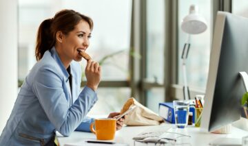 O femeie care stă la un birou și consumă alimente care accelerează procesul de îmbătrânire