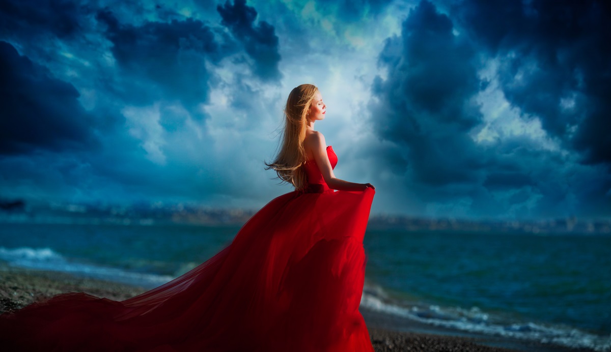 O femeie frumoasă care paortă o rochie roșie și stă în fața mării agitate