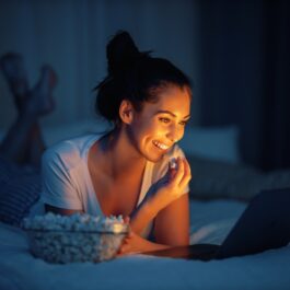 O femeie care stă în pat și mănâncă popcron în timp ce se uită la un film