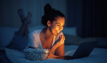 O femeie care stă în pat și mănâncă popcron în timp ce se uită la un film