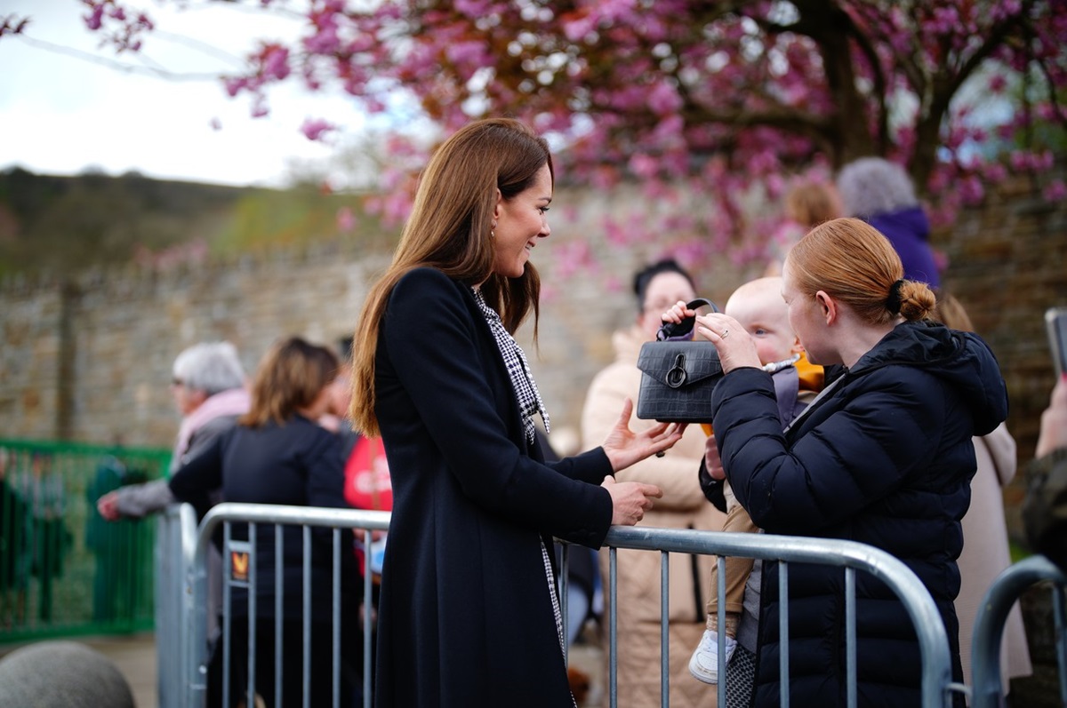 Kate Middleton în timp ce ține o poșetă și vorbește cu un bebeluș și mama acestuia