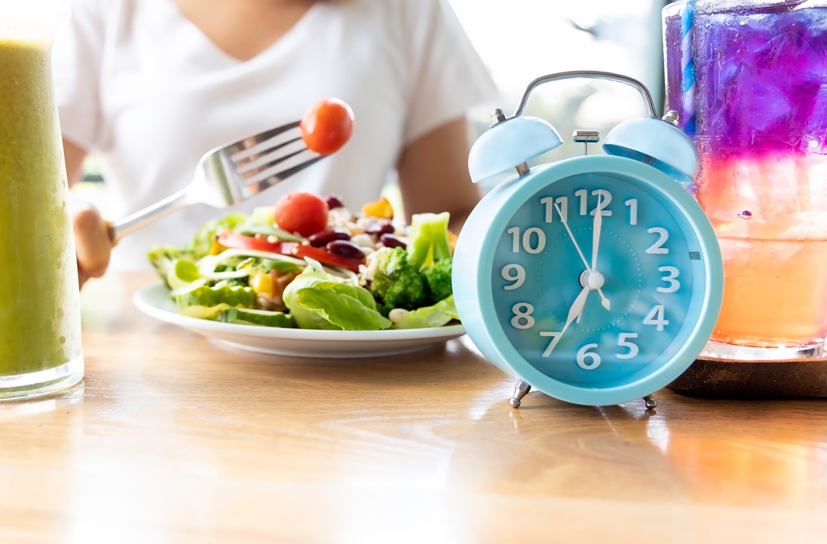 O femeie care ține postul intermitent și are alături o salată și un ceas albastru