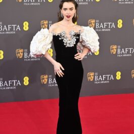 Lily Collins într-o rochie neagră cu mâneci albe în timp ce pozează pe covorul roșu de la Premiile BAFTA 2024