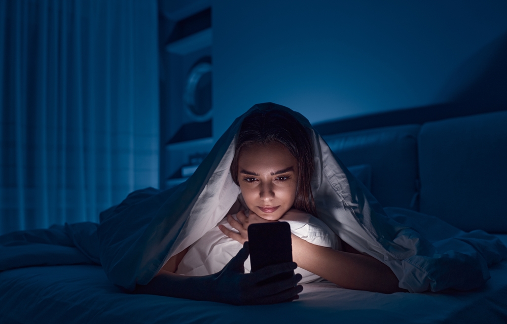 O femeie care se uită pe telefon în miez de noapte