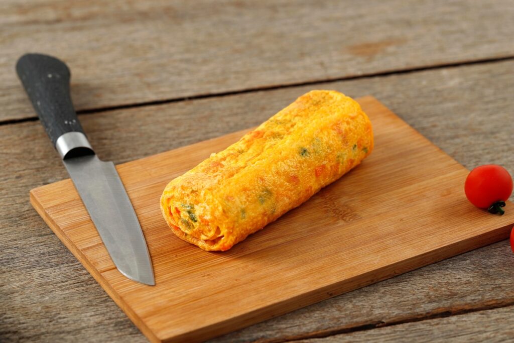 Ruladă din omletă cu morcovi și brânză pe un tocător de lemn cu cuțit