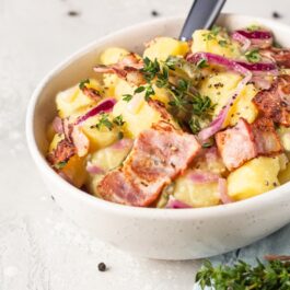 Salată caldă de cartofi, cu kaizer și ceapă roșie în bol alb cu furculiță