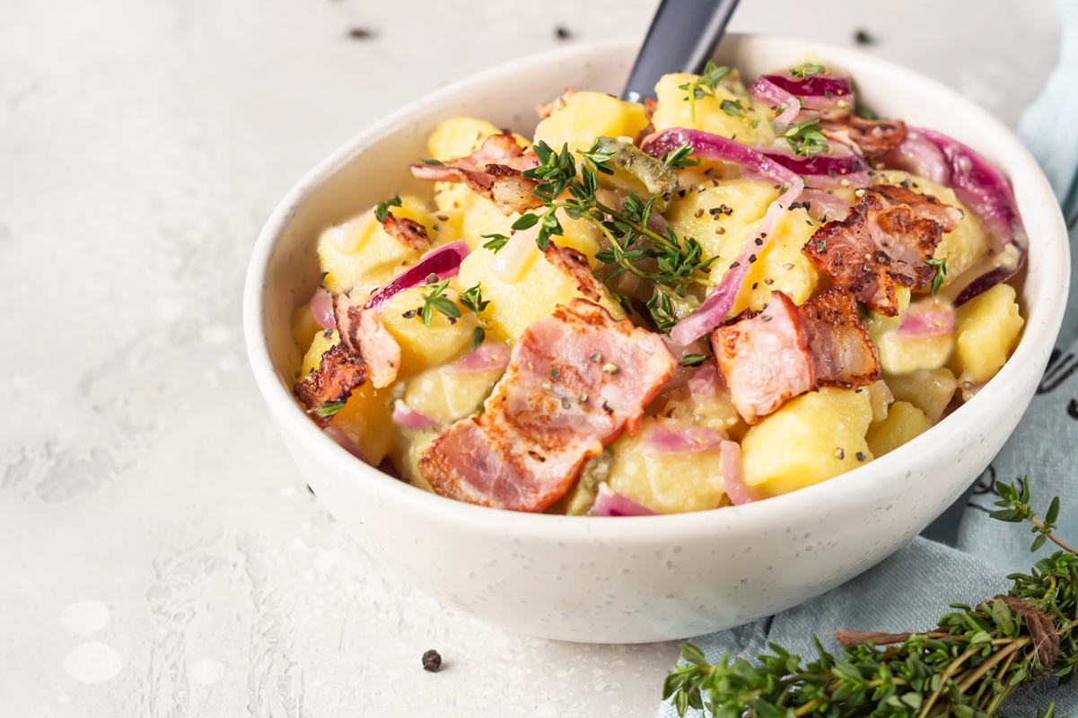 Salată caldă de cartofi, cu kaizer și ceapă roșie în bol alb cu furculiță