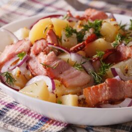 Salată caldă de cartofi, cu kaizer și ceapă roșie în bol alb
