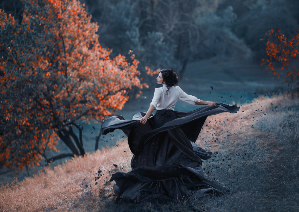 Fată frumoasă într-o rochie neagră și o bluză albă stă într-o pădure