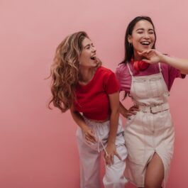 Două fete care râd pe un fundal roz, stau una lângă cealaltă
