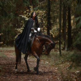 fată frumoasă îmbrăcată cu o pelerină pe un cal într-o pădure