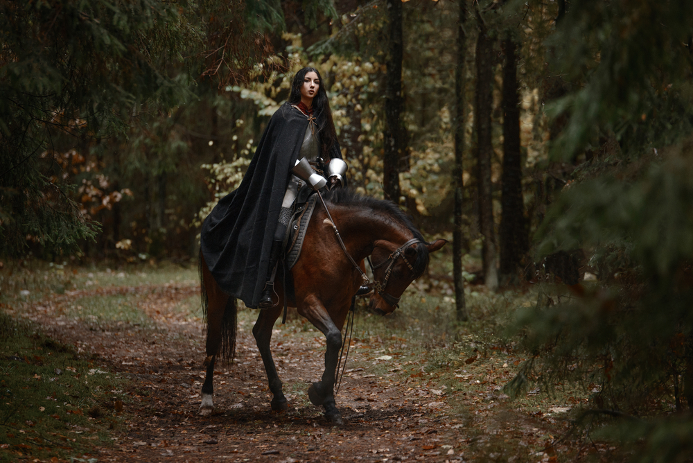 fată frumoasă îmbrăcată cu o pelerină pe un cal într-o pădure