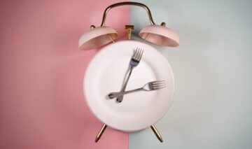 Un ceas format dintr-o farfurie, pe un fundal de roz cu gri